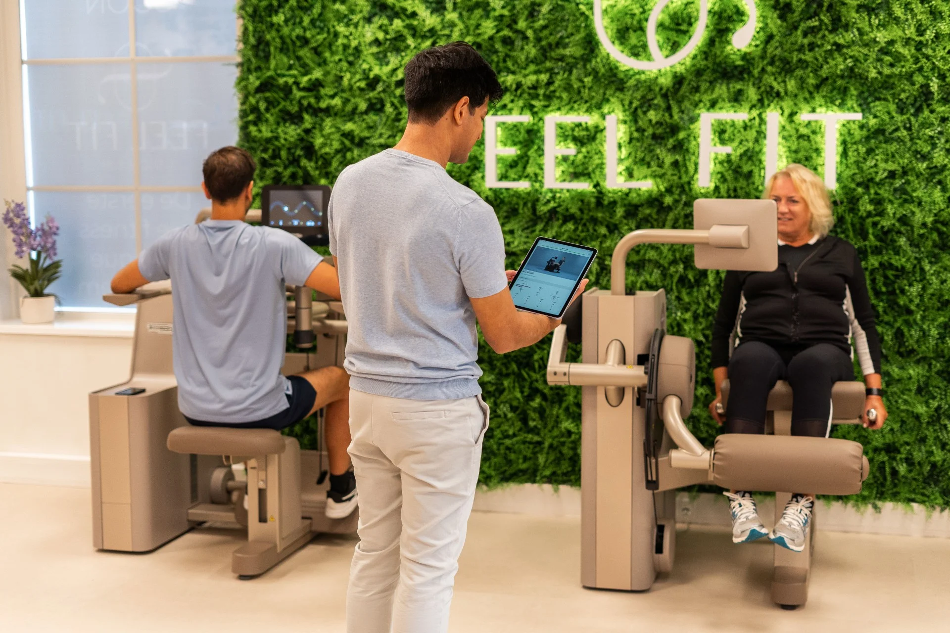 Trainer begeleidt leden met tablet tijdens training in de fitnessruimte van Feel Fit Lochem.