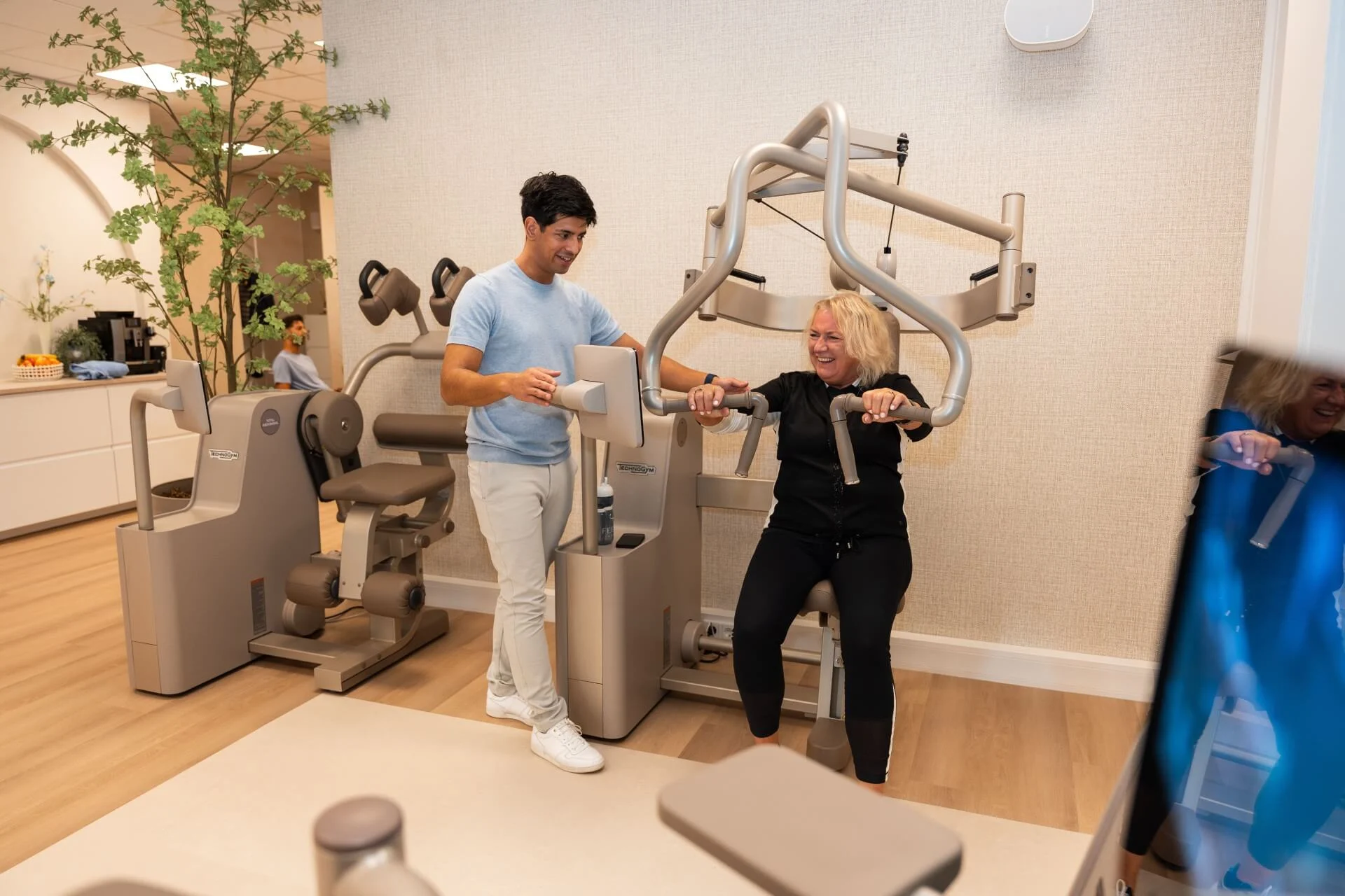 Trainer begeleidt klant bij krachttraining op Technogym Biostrength-apparaat bij Feel Fit Lochem.